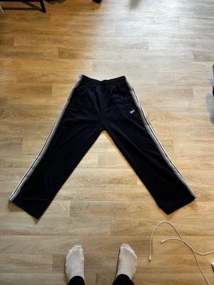Svarta mjukisbyxor från pull&bear. Vi kan förhandla - Säljer ett par svarta mjukisbyxor från pull&bearmed klassiska vita ränder längs sidorna och broderad logga på vänster ben. Byxorna har resår i midjan och raka ben. Perfekta för chill eller träning.