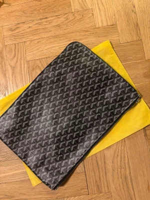 Svartmönstrad datorväska med dragkedja - Snygg datorväska i svart med vitt grafiskt mönster och dragkedja runtom. Väskan har en rektangulär form och är perfekt för att bära med sig laptopen. Kommer med en gul skyddspåse. Passar dig som vill ha en stilren och trendig look.