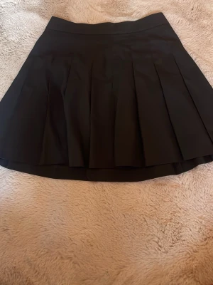 Svart kjol från Uniqlo med dragkedja - Stilren svart kjol från Uniqlo med smal passform och diskret dragkedja bak. Kjolen är tillverkad i en mjuk blandning av polyester, viskos och elastan som ger en bekväm känsla och snygg siluett. Perfekt att matcha med både t-shirt och skjorta. Använd en gång