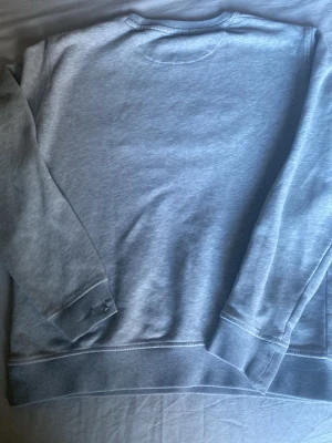 Grå sweatshirt från GANT - Säljer en klassisk grå sweatshirt från GANT med broderad logga på bröstet. Tröjan har rund halsringning, ribbade muddar vid ärmslut och nederkant samt mjukt material som känns skönt mot huden. Perfekt till jeans eller joggers.