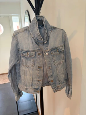 Ljusblå klassisk jeansjacka - Snygg ljusblå jeansjacka med klassisk passform och två bröstfickor med lock. Jackan har silverfärgade knappar och markerad krage. Perfekt att slänga över en hoodie eller t-shirt för en avslappnad look.