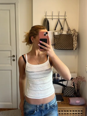 Vit virkad topp från H&M - Snygg vit virkad topp från H&M med smala axelband och rak passform. Toppen har ett luftigt, stickat mönster som ger en fräsch och somrig känsla. Perfekt att matcha med jeans eller kjol för en avslappnad look.