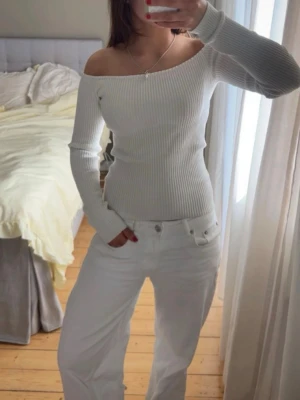 Vit ribbad offshoulder topp - Säljer en snygg vit ribbad offshoulder topp med lång ärm. Toppen är tight i modellen och har en stilren, enkel design som passar perfekt till jeans eller kjol. Materialet är stretchigt och bekvämt, vilket gör den lätt att bära hela dagen.