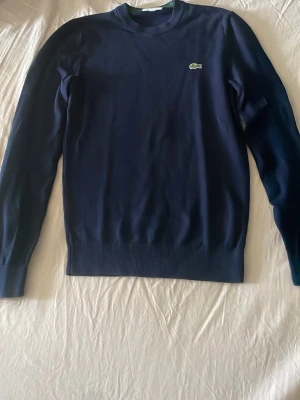 Mörkblå tröja från Lacoste - Snygg mörkblå tröja från Lacoste i regular fit. Tröjan har rund halsringning, långa ärmar och den klassiska krokodilloggan på bröstet. Perfekt för en stilren och enkel look.