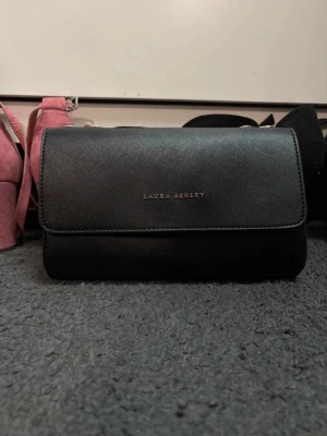 Säljer en Laura Ashley väska  - Väskan är knappt andvänd, men banden till väskan är sönder men jag har använd den som en clutchväska och tyckt de varit snyggare. De är en svart väska med guld detaljer 