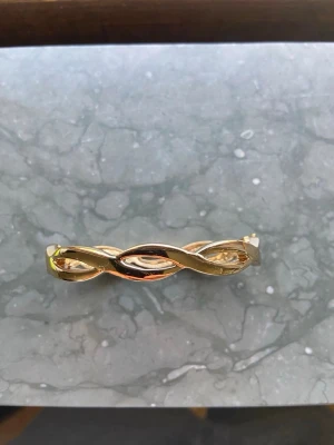 Guldigt tvinnat armband - Snyggt armband i guldfärgad metall med tvinnad design. Armbandet har en stilren och modern look som passar perfekt till din outfit. Enkel att matcha med andra smycken och accessoarer.