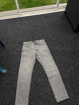 Grå tapered jeans från Jack & Jones - Snygga grå jeans från Jack & Jones i modellen Tapered/Mike. Jeansen har klassisk femficksdesign, normalhög midja och avsmalnande ben. Perfekta för en avslappnad men trendig stil.