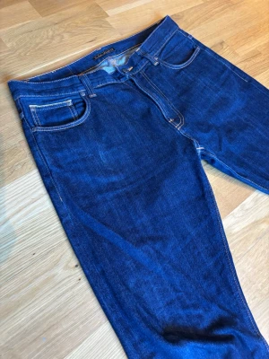 Nudie Jeans Brute Knut – Japansk Selvedge Denim - Säljer ett par exklusiva Brute Knut i Selvedge-utförande. Det här är jeans för den som uppskattar riktig denimkvalitet. Modellen har en avslappnad "anti-fit" med rymliga lår och snygg avsmalning (tapered) ner mot ankeln.  Modell: Brute Knut  Material: Selvedge Denim (orange selvedge-kant vid uppviket)  Passform: Relaxed Tapered W33 L30  Skick: Toppskick. Denna denim slits med karaktär och blir bara snyggare.  Detalj: Perfekta att bära uppvikta för att visa den klassiska selvedge-kanten.