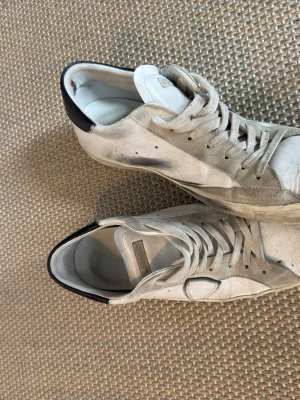 Vita Philippe Model sneakers med svart detalj - Snygga vita sneakers från Philippe Model med svarta detaljer på hälen och klassisk logga på sidan. Skorna har lågt skaft, vita snören och är tillverkade i läder och mocka. Perfekta för en stilren och trendig look. Endast lite smutsiga, men går att åtgärda med en simpel tvätt! Box och dustbag ingår självklart!