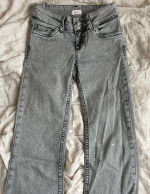 Gråa raka jeans från Nelly - Snygga gråa jeans från Nelly med raka ben och dubbla knappar i midjan. Jeansen har klassiska fem fickor och coola svarta broderade detaljer på bakfickorna. Perfekta för en trendig och avslappnad look. Skriv om ni har andra frågor!🥰 Dem är avklippta cirka 5 centimeter längst ner på benen!
