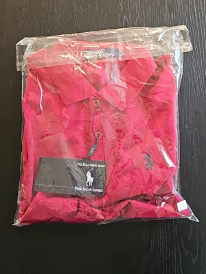 Röd pikéskjorta från Polo Ralph Lauren - Snygg röd pikéskjorta från Polo Ralph Lauren med klassisk krage och knappar framtill. Skjortan har broderad logga på bröstet och är tillverkad i bomull. Perfekt för en stilren och sportig look.