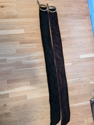 Brunt och svart sammetsbälte med ringar - Två långa bälten i sammet, ett brunt och ett svart, med stora runda metallringar som spänne. Perfekt accessoar för att ge outfiten en mjuk och cool touch. Bältena är breda och har en lyxig känsla tack vare sammetsmaterialet.75 cm långa