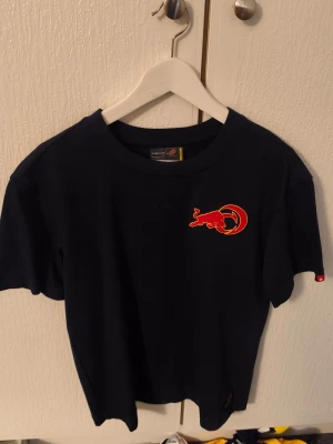 Mörkblå Red Bull Racing t-shirt - Cool mörkblå t-shirt från Red Bull Racing med deras ikoniska röda och gula logga på bröstet. Klassisk passform och rund halsringning, perfekt för dig som gillar motorsport och streetwear.