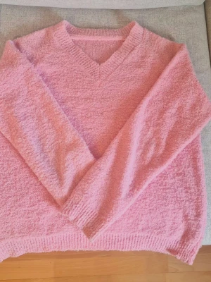 Rosa fluffig stickad tröja - Mysig rosa stickad tröja med V-ringning och långa ärmar. Tröjan är fluffig och har ribbstickade muddar vid ärmslut och nederkant. Perfekt för dig som gillar en avslappnad och trendig stil! 