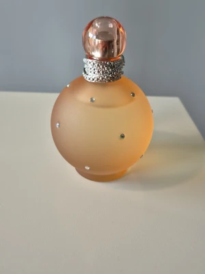 Britney Spears Naked Fantasy  - 100 ml från början, knappt använd. Har förvarats svalt & mörkt. Beskrivs med noter som följande: Toppnoter: Applejack och Black Currant ger en fräsch och sprudlande start. Hjärtnoter: En kombination av Peach, Osmanthus och Water Lily skapar ett mjukt och romantiskt hjärta. Basnoter: Cupcake, Vanilla, Apricot och Musk ger en varm och långvarig avslutning.