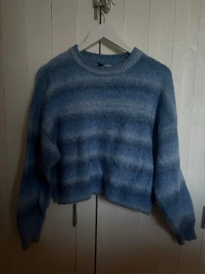 Blå stickad tröja från H&M Divided - Mysig blå stickad tröja från H&M Divided med mjuka, breda ränder i olika blå nyanser. Tröjan har rund halsringning, långa ärmar och ribbade muddar. Perfekt för kalla dagar och enkel att styla med jeans eller kjol.