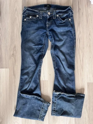 Blå bootcut jeans från True Religion - Snygga blå bootcut jeans från True Religion med klassiska kontrastsömmar och dekorativa fickor bak med knappar. Jeansen har låg midja, fem fickor och är tillverkade i denim med lätt stretch. Perfekta för en avslappnad och trendig look. Ny pris 1299kr säljs för 900kr PRIS KAN DISKUTERAS 
