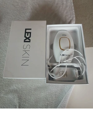 LEX SKIN IPL hårborttagningsapparat - LEX SKIN IPL hårborttagningsapparat i vit plast med gulddetaljer. Kommer med tillhörande laddare och originalförpackning. Perfekt för smidig och effektiv hårborttagning hemma.
