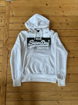 Vit hoodie från Superdry - Snygg vit hoodie från Superdry med svart och vitt tryck på bröstet och japanska tecken. Tröjan är i storlek M och endast används 4st gånger, tröjan är i mycket bra skick. Priset är diskutertbart. Skriv vid frågor och funderingar 📩🙌