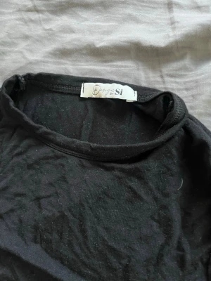 Svart kortärmad topp från Design by Si - En svart, enkel och stilren kortärmad topp från Design by Si. Toppen har en rund halsringning och är tillverkad i ett mjukt bomullsmaterial. Perfekt att matcha med jeans eller kjol för en clean look.