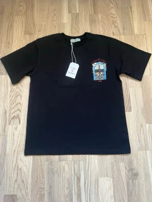 Svart t-shirt från Casablanca - Svart t-shirt från Casablanca med tryck på bröstet i färgerna blått, rött och beige. Klassisk passform med rund hals och korta ärmar. Tillverkad i mjuk bomull som känns skön mot huden. Perfekt för en clean och stilren look.