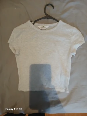 Ljusgrå t-shirt från H&M - En basic ljusgrå t-shirt från H&M i mjuk bomull. Modellen är kortärmad med rund halsringning och har en enkel, clean look som passar till det mesta. Perfekt att matcha med jeans eller shorts.