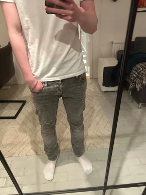 Grå slim fit jeans  - Snygga grå slim fit jeans med tvättad effekt och klassiska fem fickor. Jeansen har en modern passform som sitter tajt längs benen och detaljerade sömmar i storlek 29/30. Perfekta för dig som gillar en stilren och trendig look.