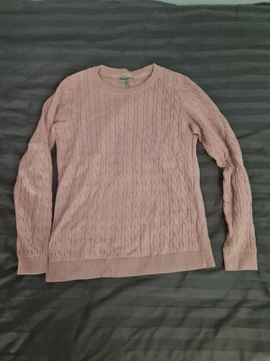 Ljusrosa kabelstickad tröja från Basic You - Ljusrosa kabelstickad tröja från Basic You i ekologisk bomull. Tröjan har rund halsringning, långa ärmar och ribbade muddar vid ärmslut och nederkant. Perfekt för dig som gillar en enkel och stilren look.