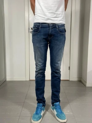 Replay Anbass Jeans - Säljer ett par blå slim fit jeans med snygga slitningar och tvättade detaljer. Jeansen har klassisk femficksdesign, normal midja och smal passform hela vägen ner. Perfekta för en avslappnad och trendig look.