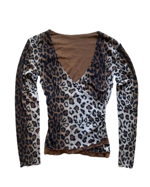 y2k vintage Leopardmönstrad omlottopp brun - Snygg omlottopp med leopardmönster i bruna och svarta toner. Djup v-ringning och långa ärmar. Ingen storlek eller märke. Men passar en S. 