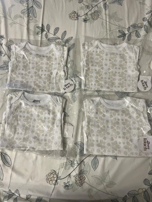 Libero Touch vita babytröjor med blommor - Fyra vita babytröjor från Libero Touch med ljusbeige blommönster. Tröjorna har rund hals och är tillverkade i mjukt material, perfekta för små barn. Säljs i originalförpackning med etikett kvar.
