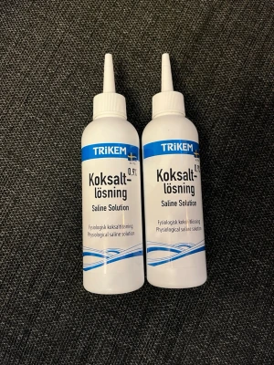 Koksaltlösning 0,9% från Trikem - Två flaskor koksaltlösning 0,9% från Trikem. Flaskorna är vita med blå etikett och har smal pip för enkel dosering. Perfekt för rengöring eller sköljning. Text på både svenska och engelska.