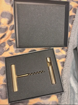 Lyxig vinöppnare i mässing med etui - Snygg vinöppnare i metall med guldfärgad finish, levereras i en elegant svart presentask med guldfärgad och vit logotyp på locket. Handtaget är cylinderformat och korkskruven har en klassisk spiralform. Perfekt till vinälskaren som gillar stilrena detaljer.rostfritt 