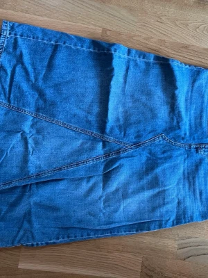 Blå jeanskjol i A-linjeform - Snygg blå jeanskjol i klassisk A-linjeform med dekorativa sömmar framtill. Kjolen har en enkel design utan synliga knappar eller dragkedja och är tillverkad i denim. Perfekt för dig som gillar en tidlös och avslappnad stil.