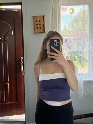 Lila och vit tubtopp - Säljer en snygg tubtopp i lila med vit kant upptill. Toppen är axelbandslös och har en croppad passform som sitter tight mot kroppen. Perfekt för varma dagar och enkel att matcha med jeans eller kjol.