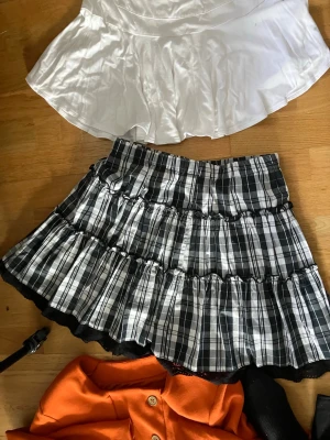 Svartvit rutig kortkjol med volang - En svartvit rutig kortkjol med volangkant och flera lager. Kjolen har en klassisk plisserad look och är perfekt för dig som gillar en trendig och ungdomlig stil.