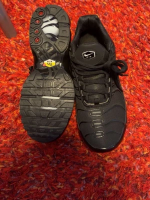 Svarta Nike Air sneakers - Snygga svarta Nike Air sneakers med klassisk logga på plösen och innersulan. Skorna har en sportig design med mönstrad sula och ovandel i textil och syntet. Perfekta för dig som gillar streetwear och vill ha en stilren look.