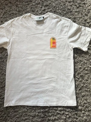 Vit Casa Blanca t-shirt med tryck - Säljer en vit t-shirt från Casa Blanca med färgglatt grafiskt tryck fram och stort tryck på ryggen. T-shirten har rund hals och korta ärmar. Perfekt för dig som gillar stilrena plagg med en twist. Materialet är mjuk bomull.