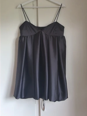 Svart satin klänning med smala band - Snygg svart kort klänning i satin med tunna axelband och lätt rynkad byst. Klänningen har en luftig passform och smock i ryggen för extra komfort. Perfekt för dig som gillar minimalistisk och stilren design. Prislappen kvar! 