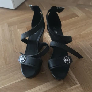 Svarta sandaler från Michael Kors - Snygga svarta sandaler från Michael Kors med breda remmar och silverfärgad MK-logga framtill. Passar någon med Stl. 39 oxå