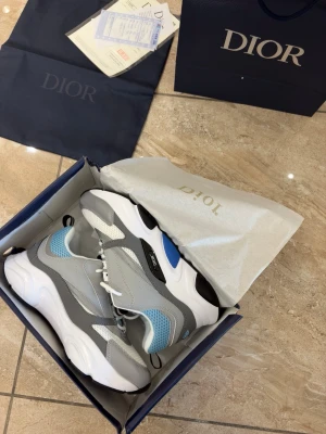  B22 sneakers i grått och blått - Snygga B22 sneakers i grått, vitt och ljusblått med meshpaneler och detaljer i läder. Skorna har chunky sula, vita skosnören och svart logotyp på sidan. Perfekta för dig som gillar exklusiva och trendiga sneakers.