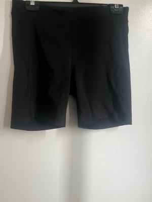 Svarta cykelshorts från OTP - Svarta cykelshorts från OTP med midwaist passform. De är tillverkade i ett stretchigt syntetmaterial som passar perfekt för träning. Enkla och stilrena utan synliga detaljer eller mönster.