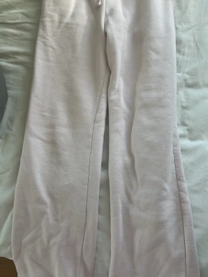 Ljusrosa mjukisbyxor med raka ben - Säljer ett par ljusrosa mjukisbyxor med raka ben och resår i midjan. Byxorna har dragsko och är tillverkade i ett mjukt och bekvämt material, perfekt för en avslappnad stil. Passar dig som gillar enkel och clean look.