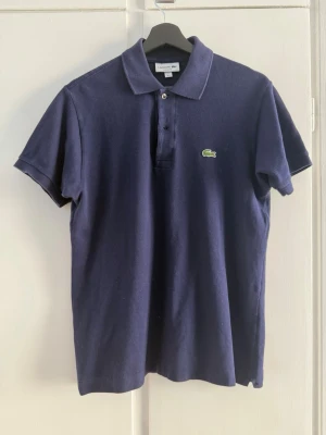 Lacoste piké - Klassisk marinblå pikétröja från Lacoste med korta ärmar och krage. Storlek S men passar M. Skitsnyggt alternativ till sommaren! Priset kan diskuteras vid snabb affär!