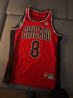 Chicago Basketlinne  - Snyggt röd basketlinne från FSBN med svart och vit kant, stort CHICAGO-tryck och nummer 8 på framsidan. Perfekt för basket eller streetwear. Atletisk passform och tillverkad i lätt material, perfekt för sommar. Passar för dig som gillar basket. 