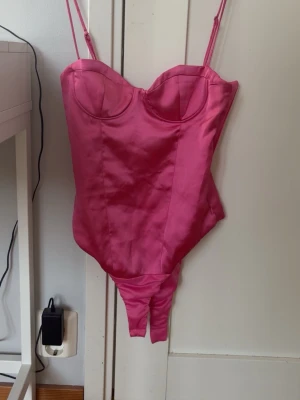 Rosa satinbody från zara - Snygg rosa body i glansigt satinmaterial med tunna justerbara axelband och formpressade kupor. Perfekt för dig som vill ha en feminin och trendig look. Bodyn har en figurnära passform och klassisk skärning nedtill.