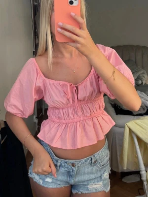 Korall rosa topp med puffärmar - Supersöt rosa  blus med puffärmar och volang nedtill. Toppen har en söt knytning framtill och kan bäras både på axlarna eller offshoulder. Perfekt för sommarens alla tillfällen🙌🫰