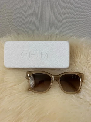 Beige solglasögon från CHIMI - Stilrena solglasögon från CHIMI med transparent beige båge och fyrkantig form. Glasen är tonade i brunt och bågarna har en snygg CHIMI-logga på sidan. Väldigt bra kvalitet då dom knappt är andvända🤎