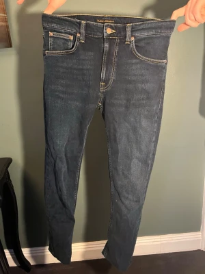 Mörkblå slim fit jeans från Nudie - Säljer ett par mörkblå skinny jeans från Nudie Jeans med klassiska kontrastsömmar och femficksmodell. Jeansen har en snygg passform och är tillverkade i stretchigt denimtyg för extra komfort. Nudie-logga på bakfickan och patch bak i midjan. Nypris ca 1600 kr 