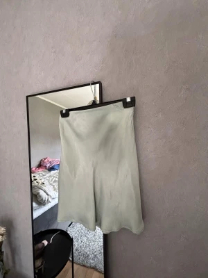 Ljusgrön satin kortkjol - Snygg ljusgrön kortkjol i satinliknande material med lätt glansig finish. Kjolen har en enkel och stilren design utan synliga detaljer eller mönster, perfekt för att skapa en trendig look.